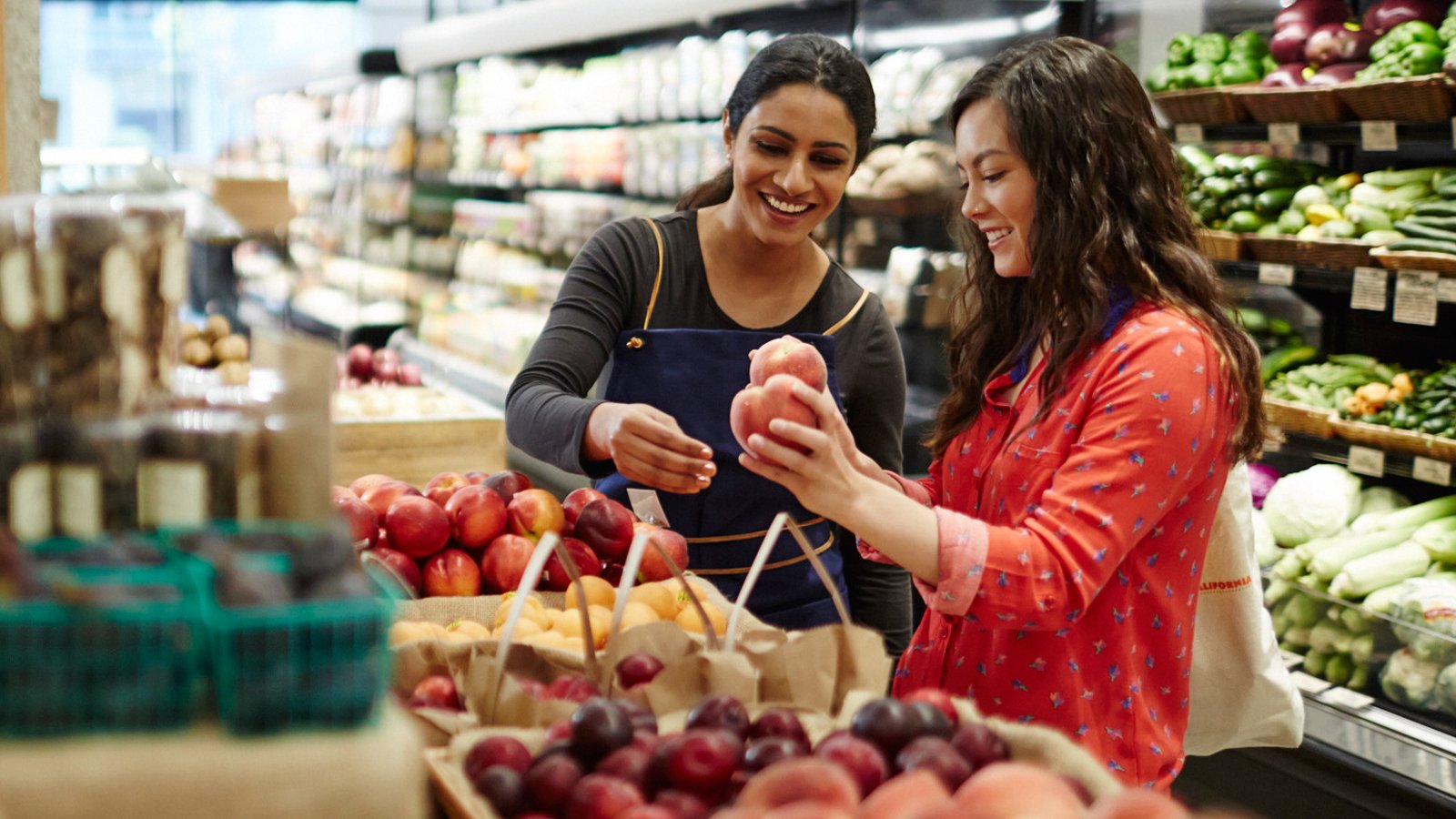 Two women at a grocery store conversing in the produce section.