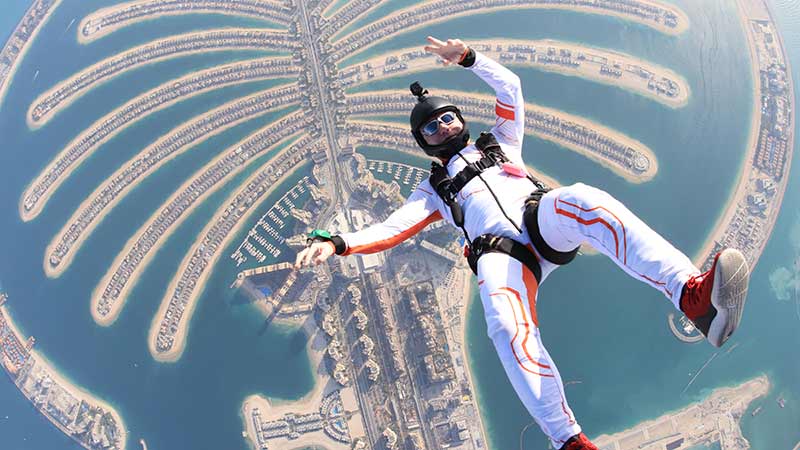 Air beach jump. Freedom as a way of life. Parachutist performs an acrobatic trick in the Dubai air tourism. Parachutist in white suit. Skydiver is in air free fall.